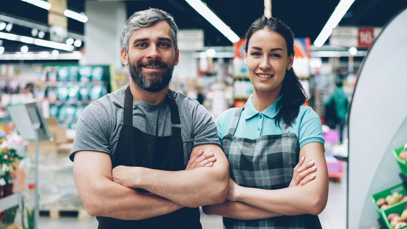 Two store colleagues in aprons smiling in a supermarket aisle